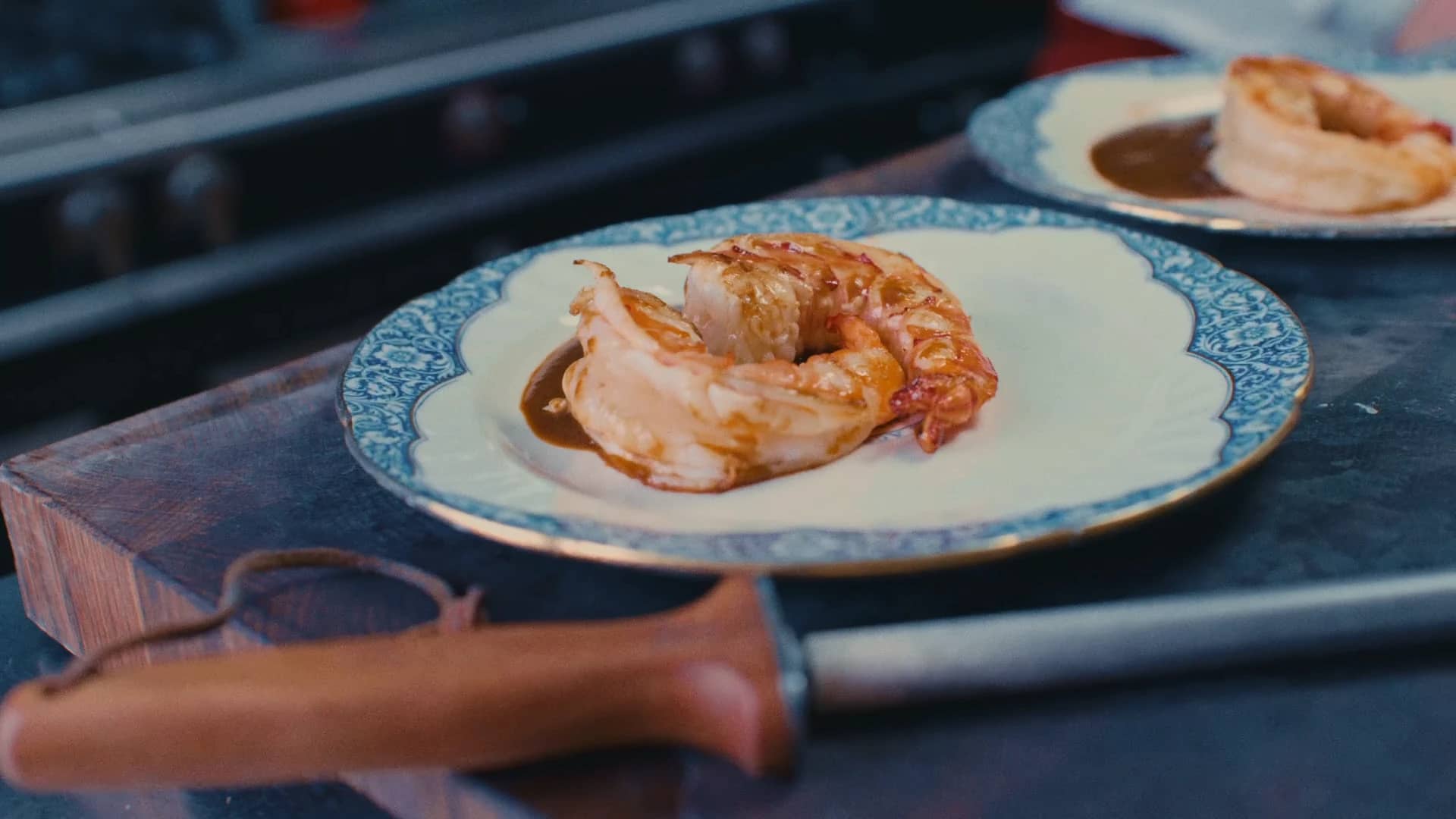 Assiette dressée par Andres Oppenheim : queues de crustacés et leur sauce sur porcelaine au bord bleu, dans la cuisine de la maison à Puidoux