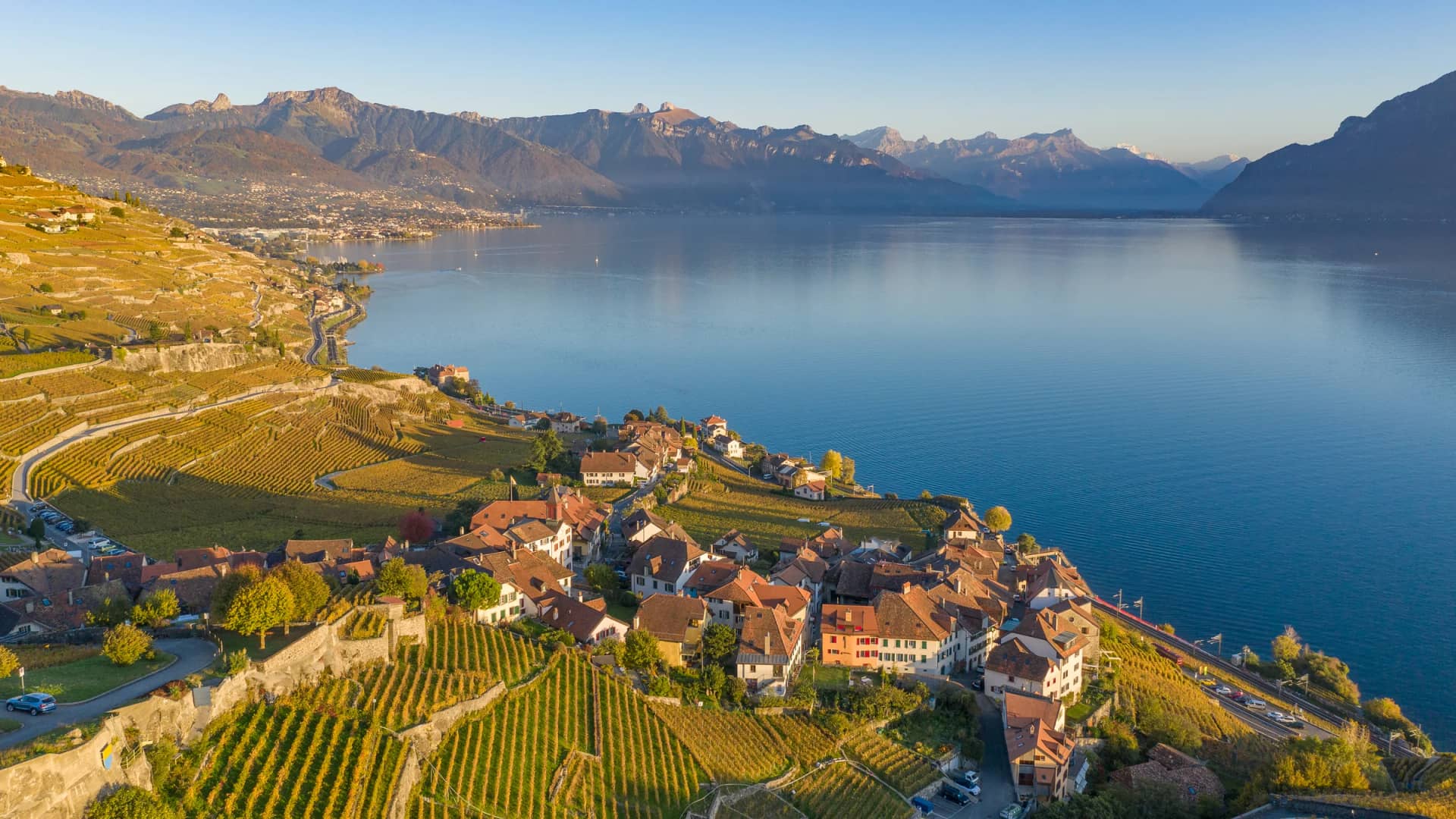 Les vignes dorées des terrasses de Lavaux en automne, un village vigneron et le Léman face aux Alpes