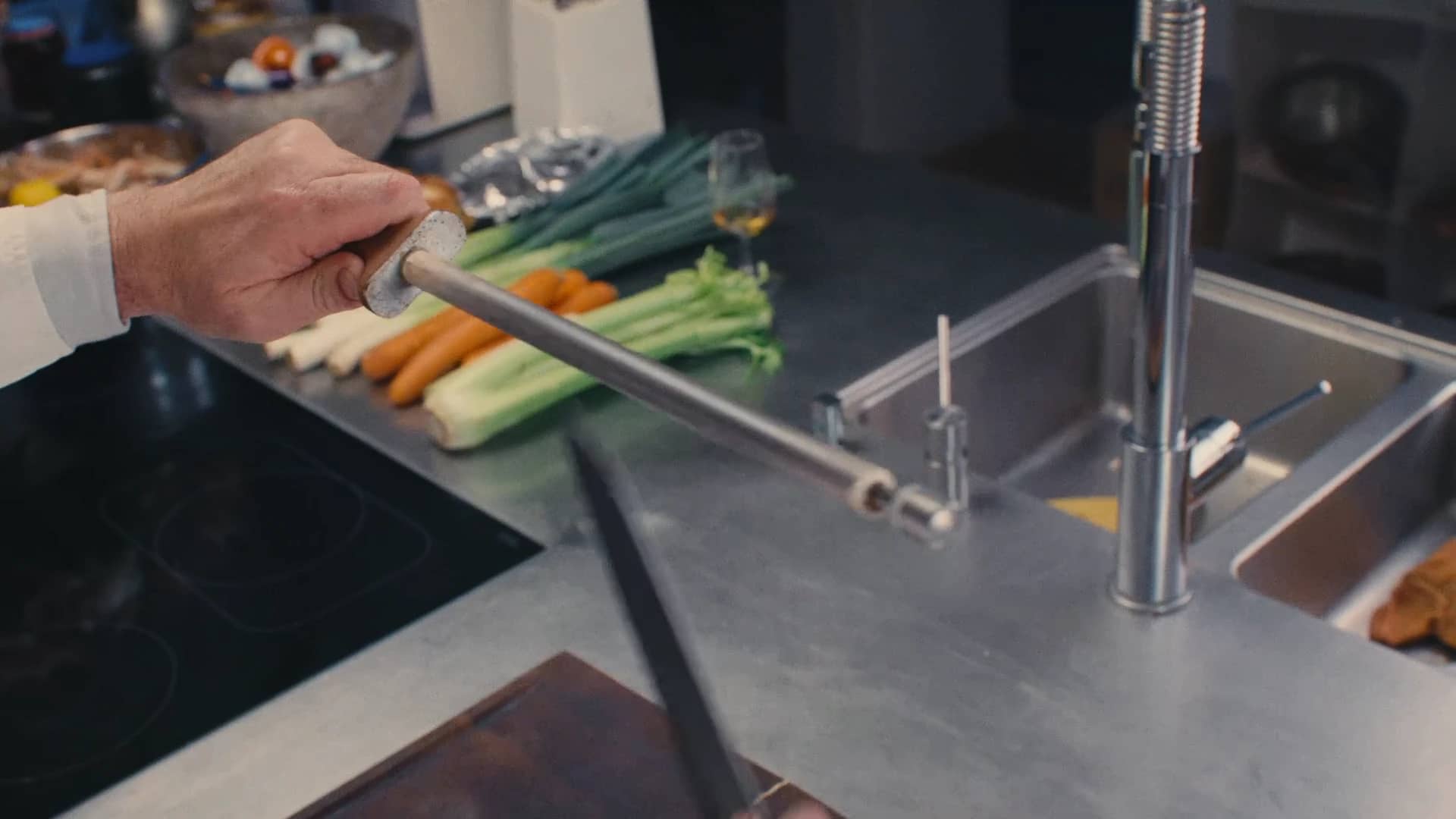 Andres Oppenheim aiguise son couteau au fusil, au-dessus de légumes posés près de l'évier, dans la cuisine de la maison à Puidoux