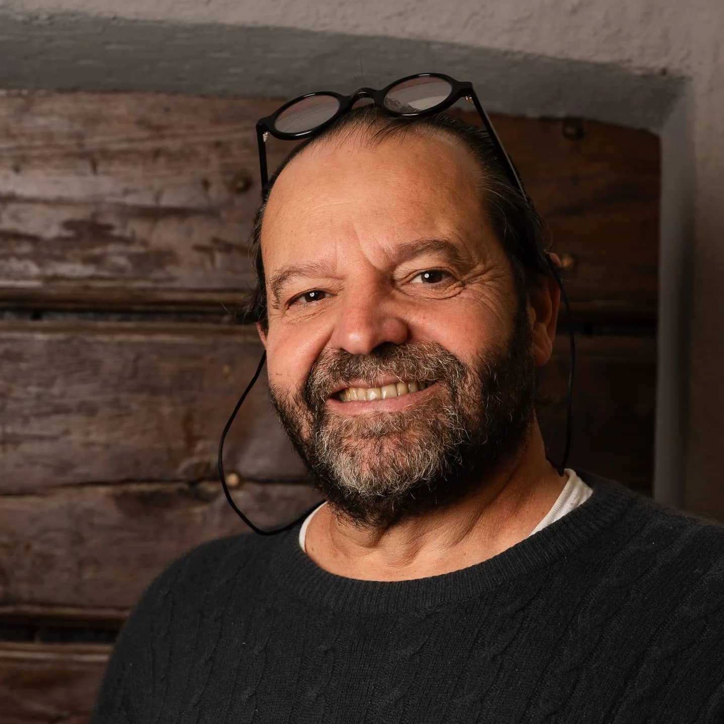 Andres Oppenheim sourit, ses lunettes relevées sur la tête, devant une vieille porte en bois