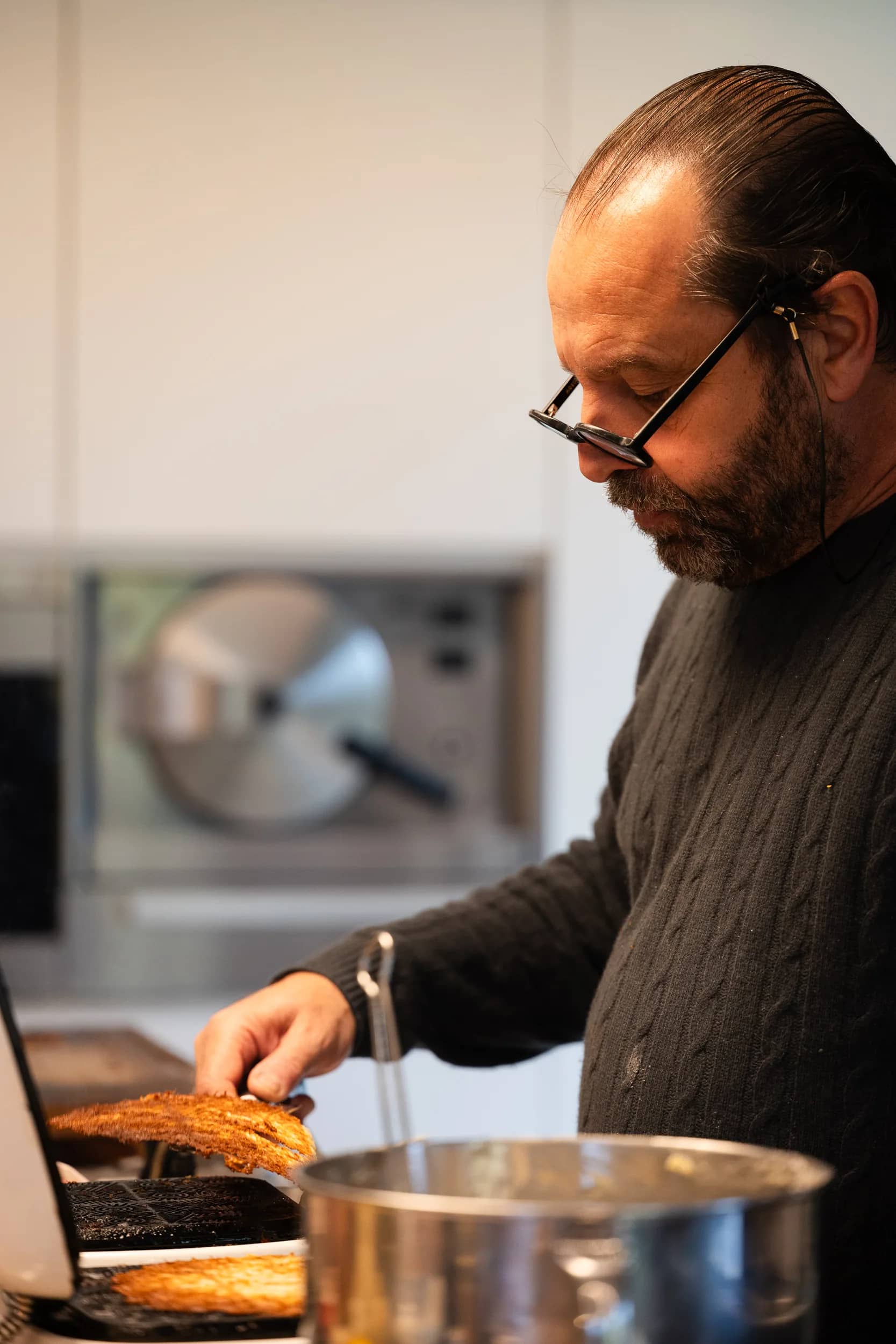 Andres Oppenheim soulève une galette dorée du fer à bricelets ouvert, à côté d'une casserole en inox, dans sa cuisine