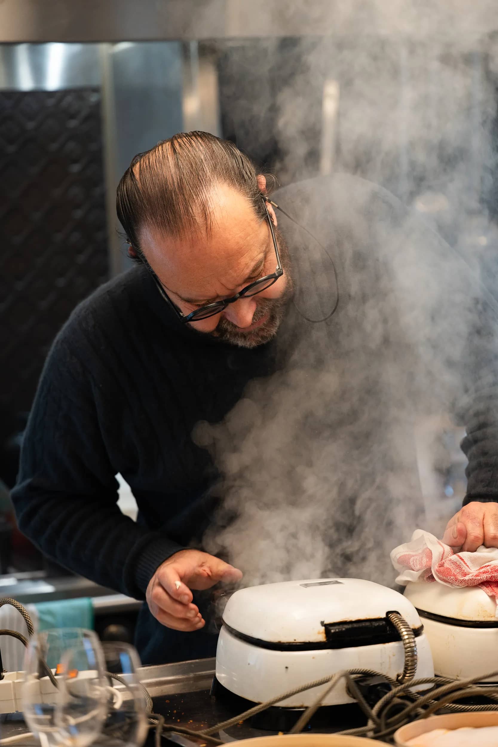 Andres Oppenheim penché sur un fer à bricelets fumant, la vapeur lui monte au visage