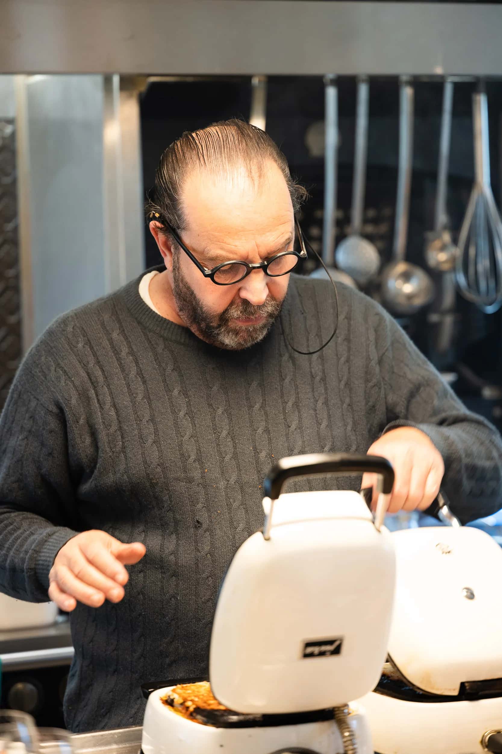Andres Oppenheim soulève le couvercle d'un fer à bricelets, dans sa cuisine