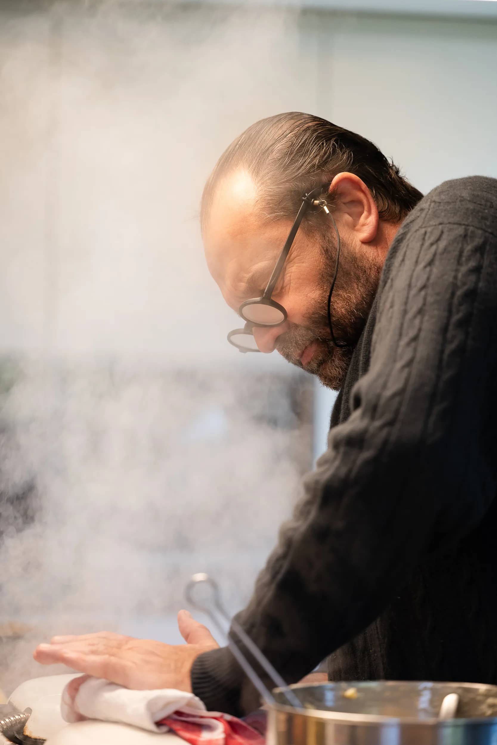 Andres Oppenheim, de profil, penché sur son plan de travail dans un nuage de vapeur, dans la cuisine de la maison
