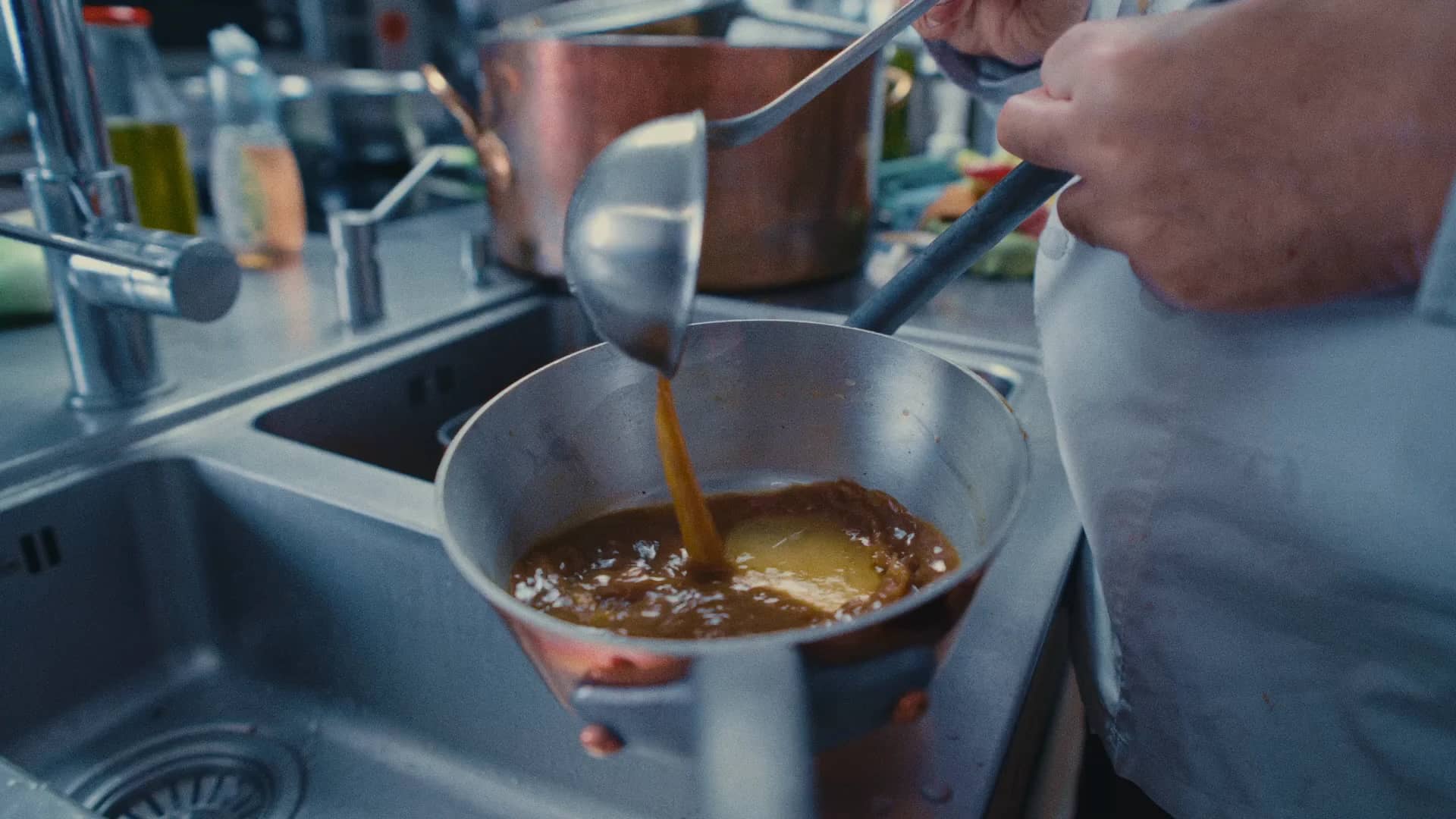 Andres Oppenheim verse une sauce à la louche dans une casserole, devant les cuivres de la cuisine de la maison