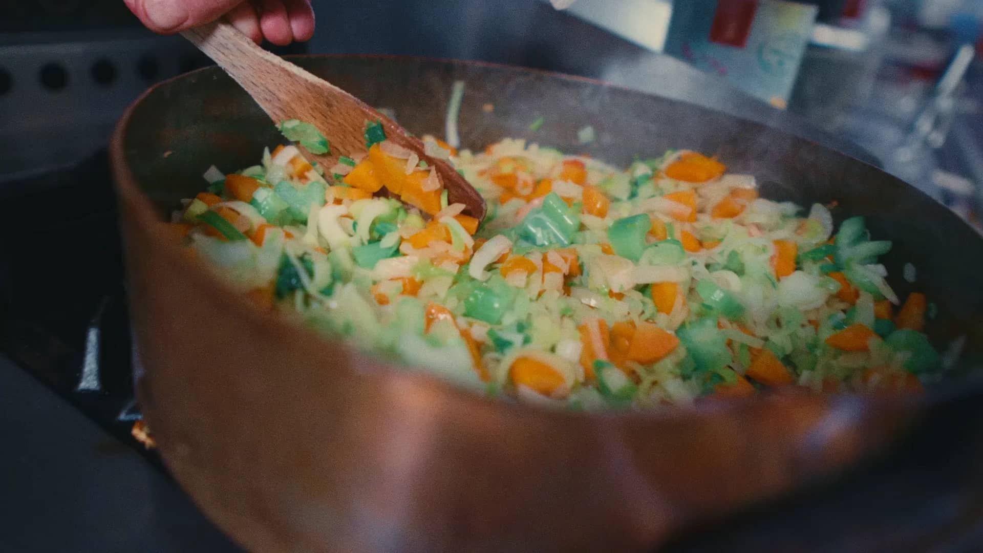 Une sauteuse en cuivre pleine de légumes coupés, remués à la spatule en bois sur le fourneau de la maison