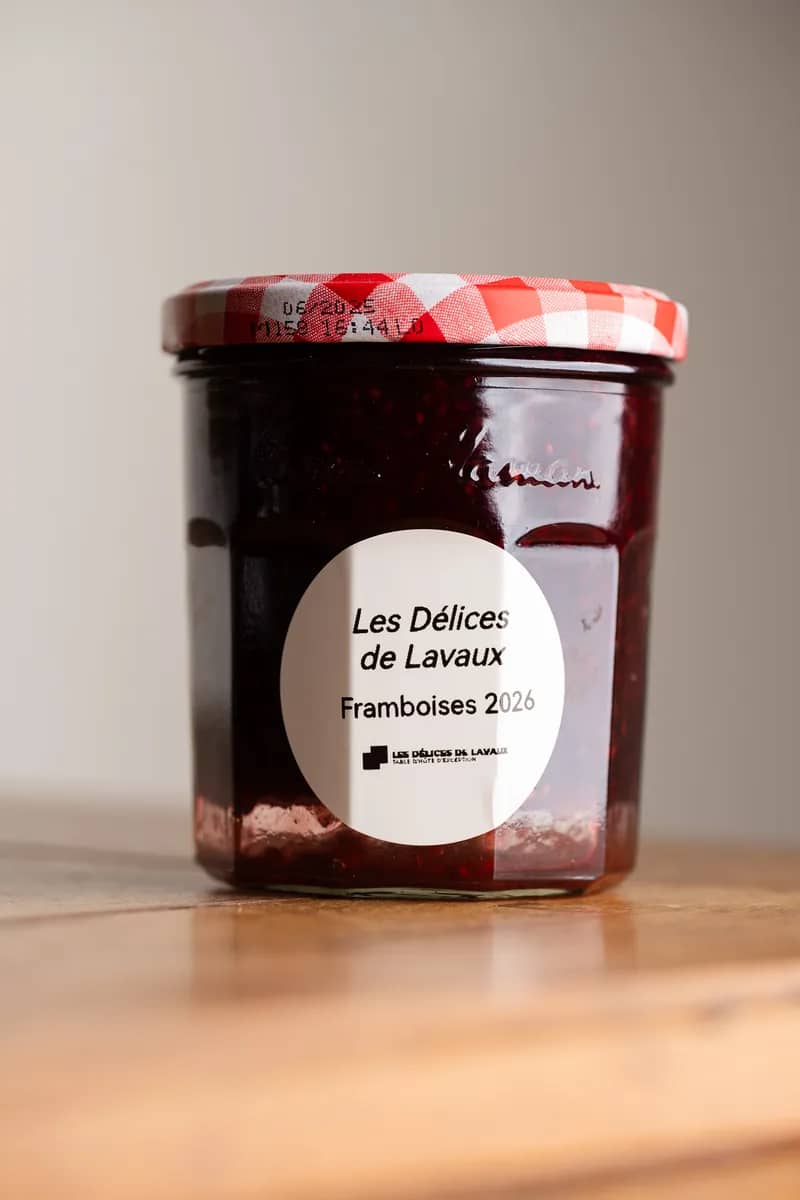 Un pot de framboises 2026 à couvercle vichy rouge, étiquette ronde, sur une table en bois