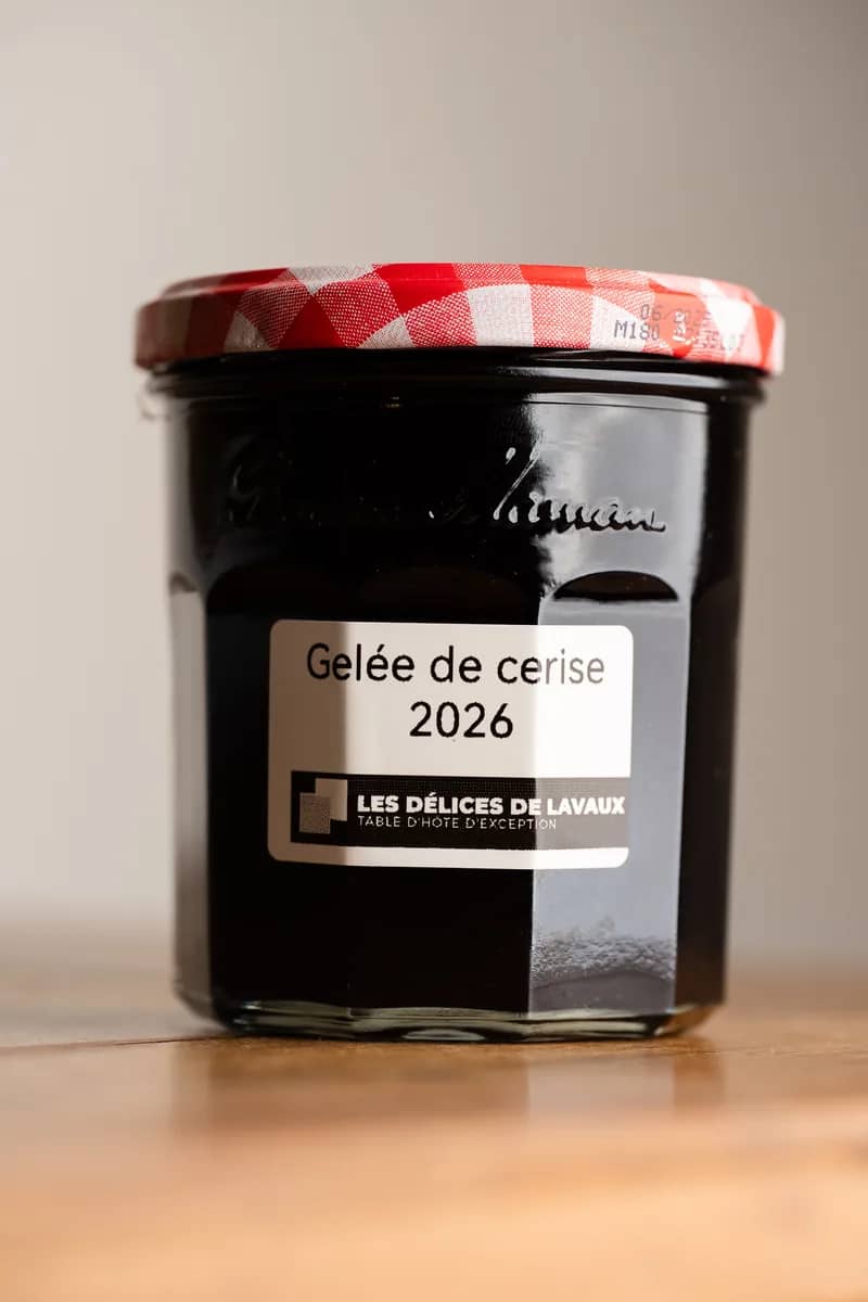 Un pot de gelée de cerise 2026, étiquette rectangulaire, couvercle vichy rouge, sur une table en bois