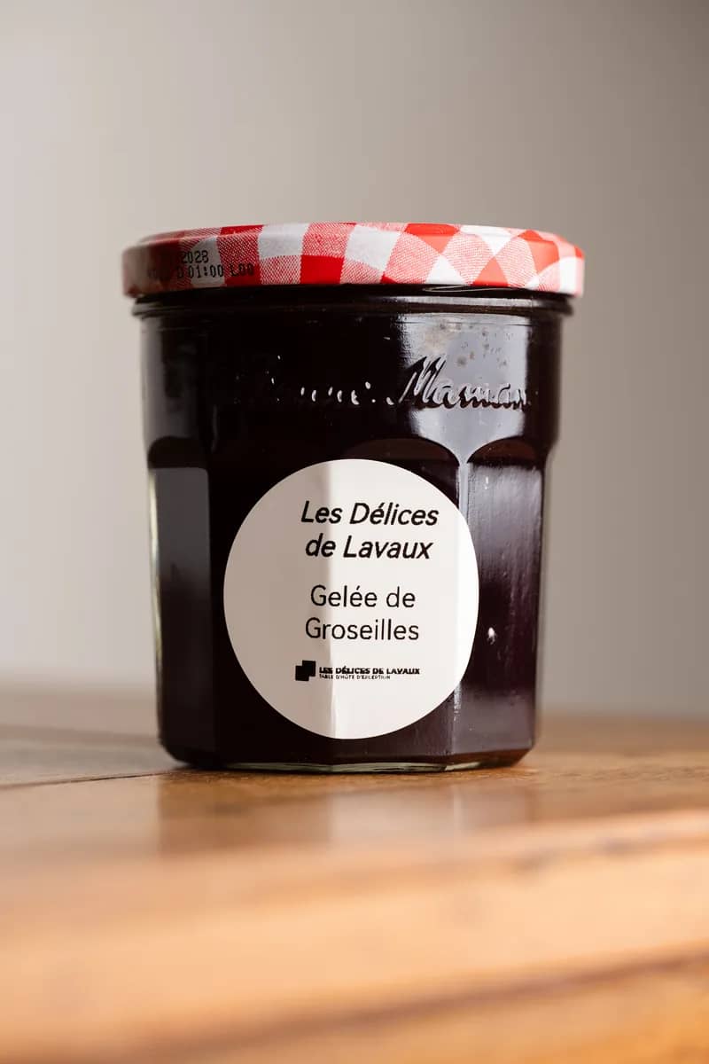 Un pot de gelée de groseilles à couvercle vichy rouge, étiquette ronde, sur une table en bois