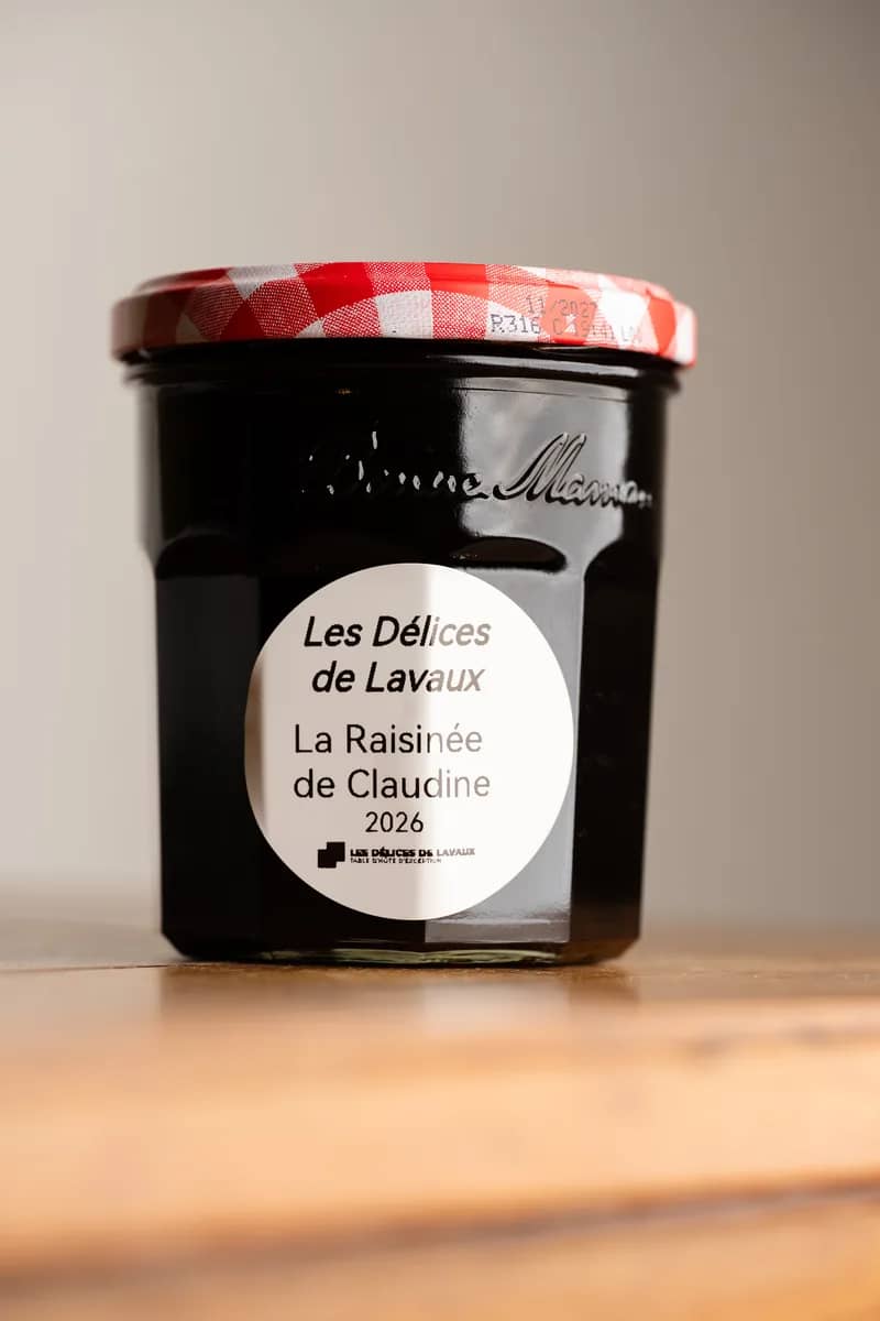 Un pot de raisinée, millésime 2026, à l'étiquette ronde et au couvercle vichy rouge, sur une table en bois