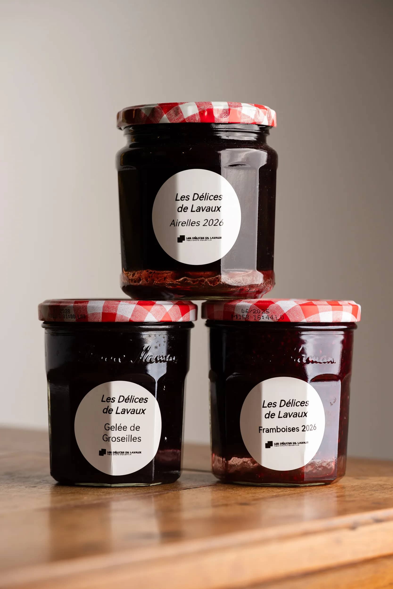 Trois pots de la maison à couvercle vichy rouge, empilés : airelles, gelée de groseilles et framboises 2026