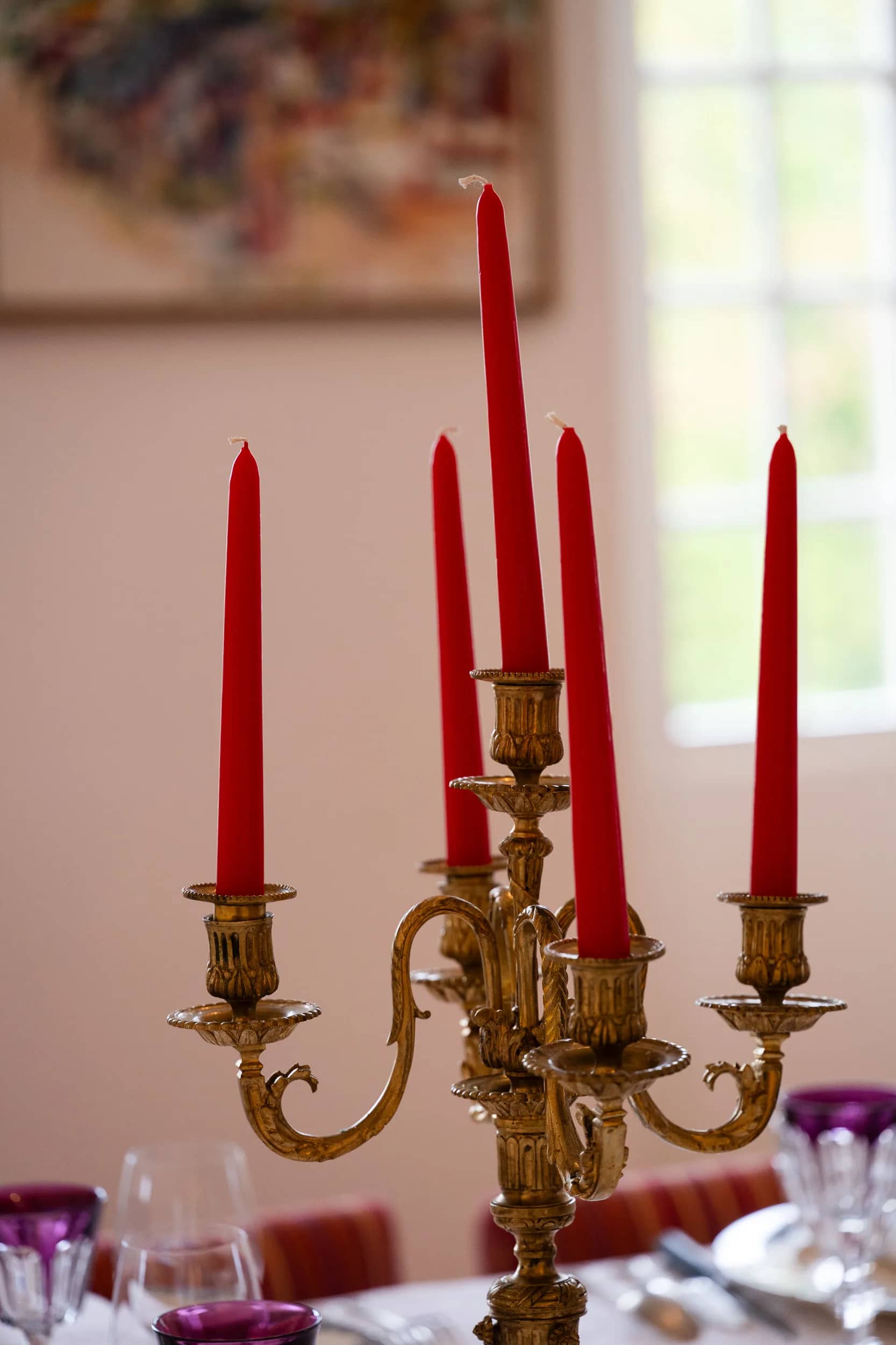 Un chandelier doré aux bougies rouges, devant un tableau et une fenêtre de la salle à manger de la maison
