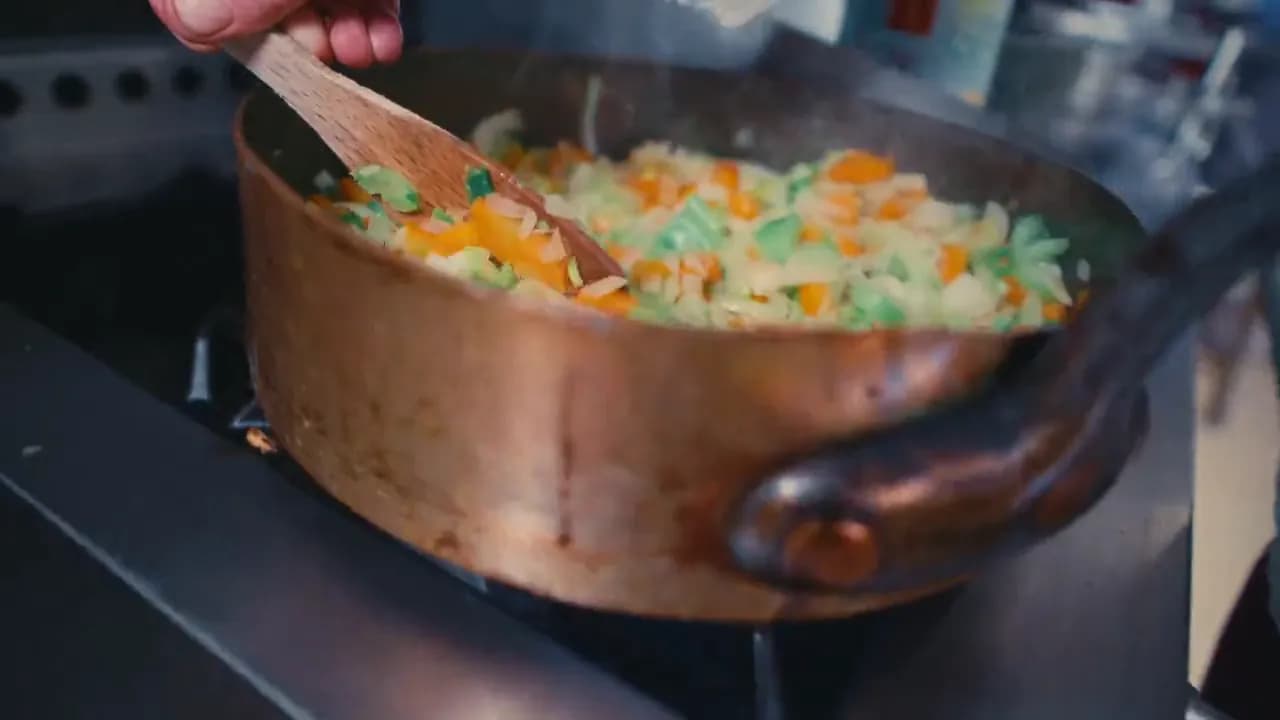 Andres Oppenheim remue des légumes dans une sauteuse en cuivre, au fourneau de la cuisine de la maison, à Puidoux