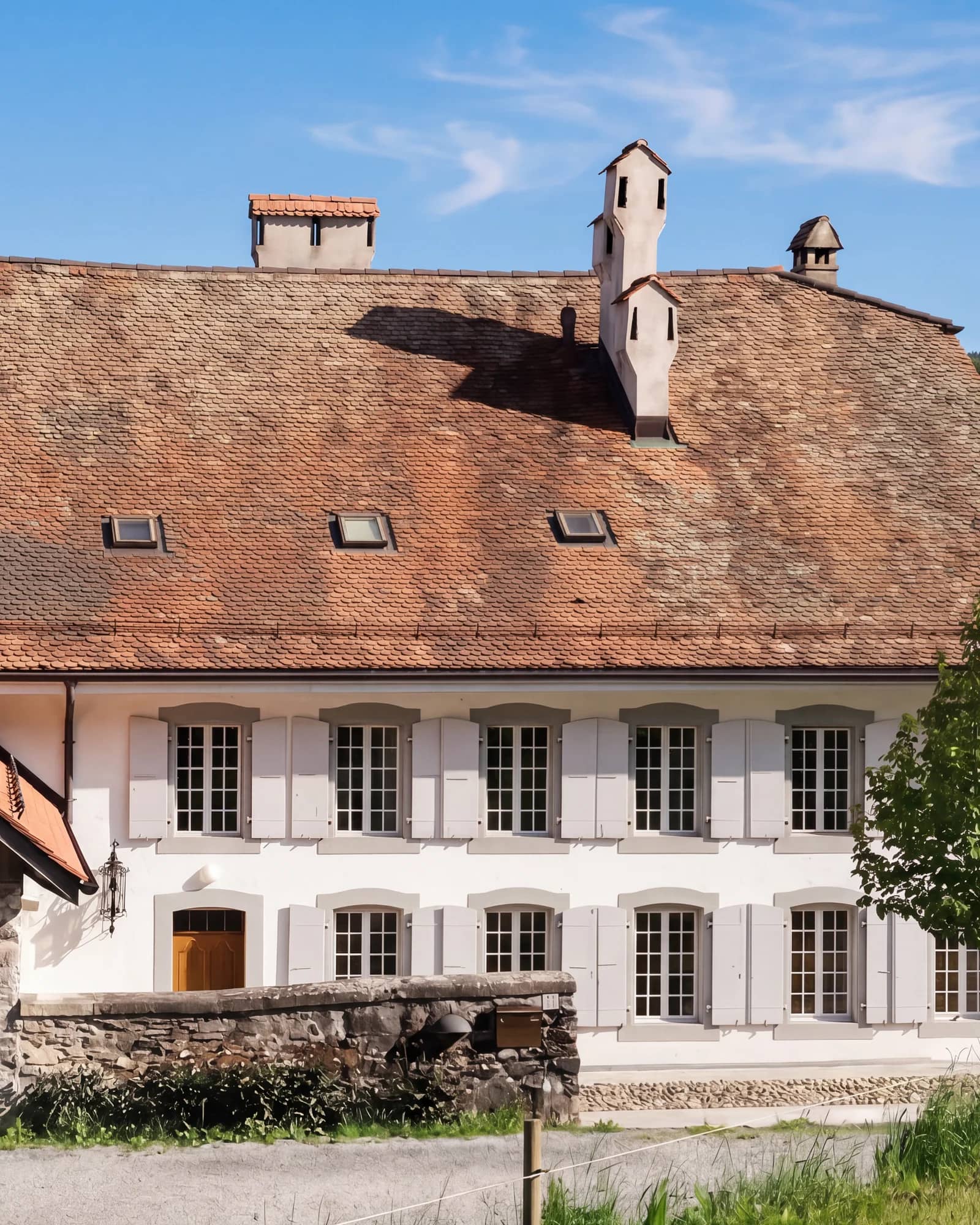La façade côté cour de la maison de maître, où arrivent vos invités : porte en bois, volets gris et grand toit de tuiles anciennes