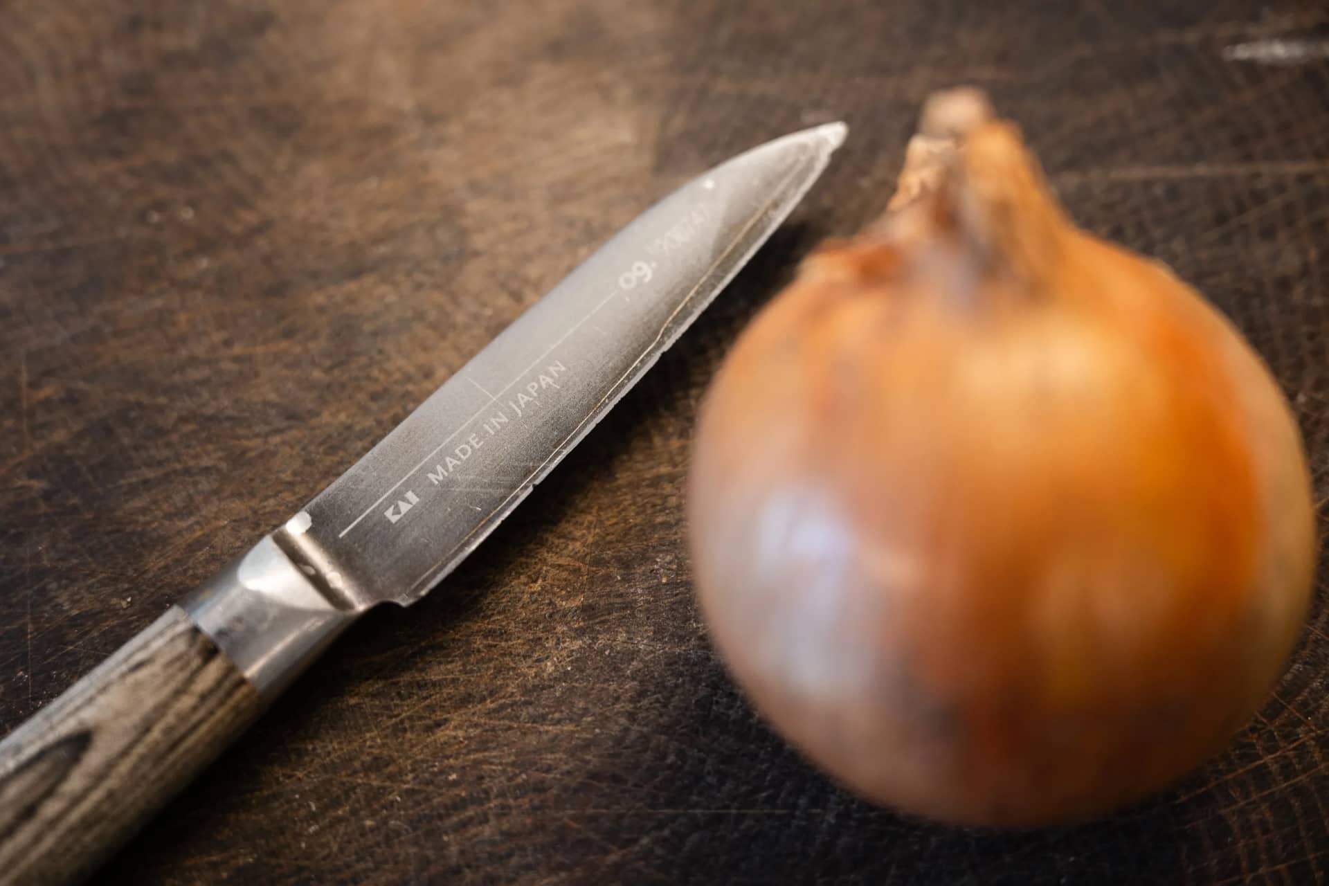 Un couteau de cuisine et un oignon doré sur une vieille planche en bois sombre
