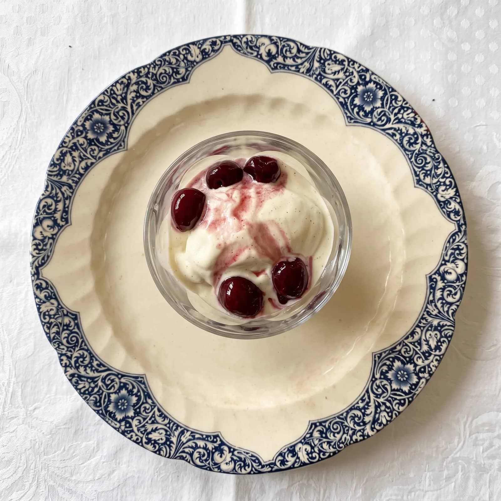 Vue de dessus, une coupe en verre de crème et de meringue aux cerises noires, sur une assiette en porcelaine à frise bleue