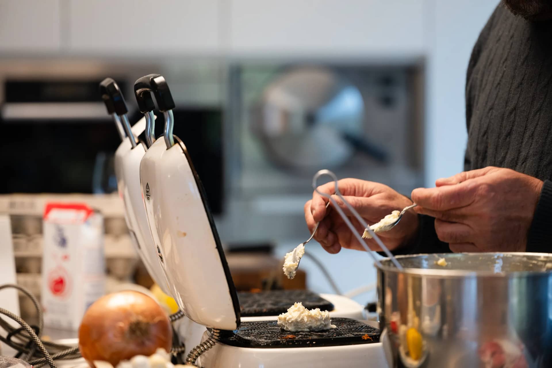 Les mains d'Andres Oppenheim, une cuillère dans chaque main, au-dessus d'un fer à bricelets ouvert