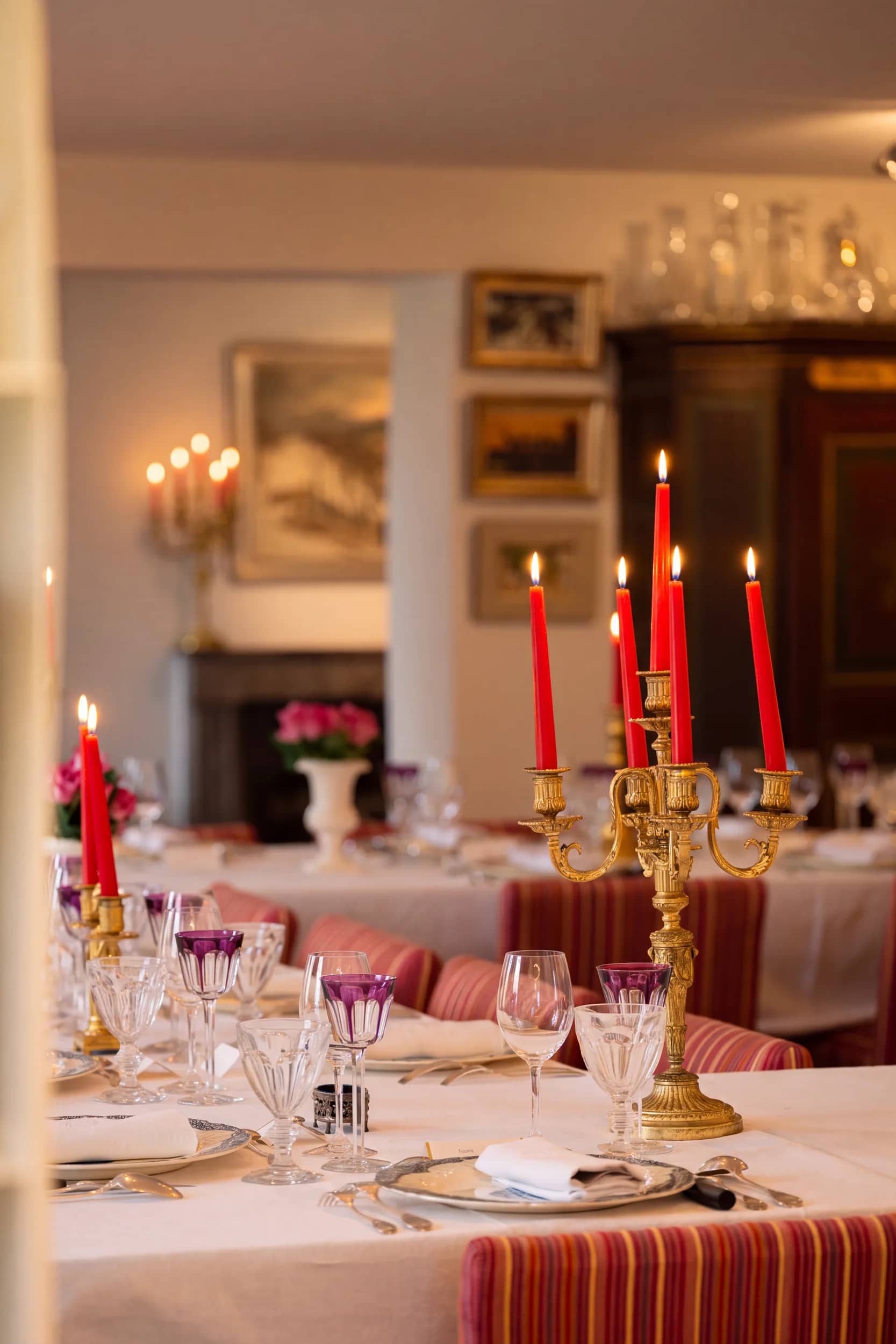 Le soir dans la salle à manger : les bougies rouges du grand chandelier doré sont allumées, les verres en cristal améthyste brillent, au fond les tableaux et l'armoire peinte dans la lumière des bougies