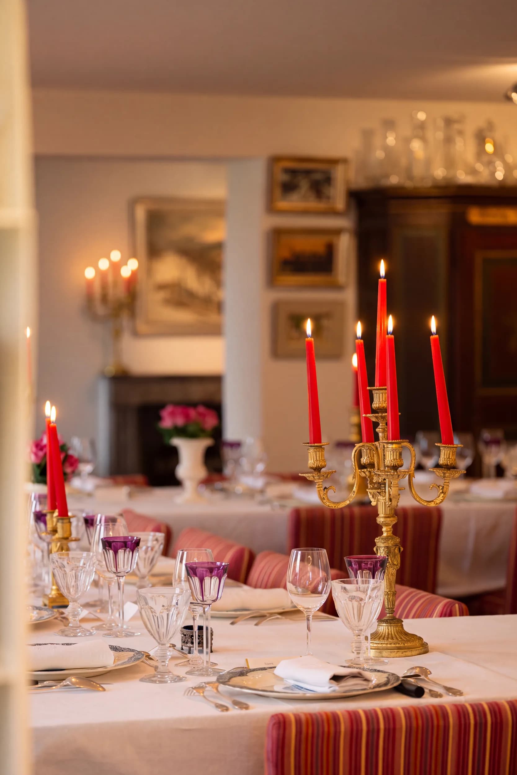 Le soir dans la salle à manger : les bougies rouges du grand chandelier doré sont allumées, les verres en cristal améthyste brillent, au fond les tableaux et l'armoire peinte dans la lumière des bougies