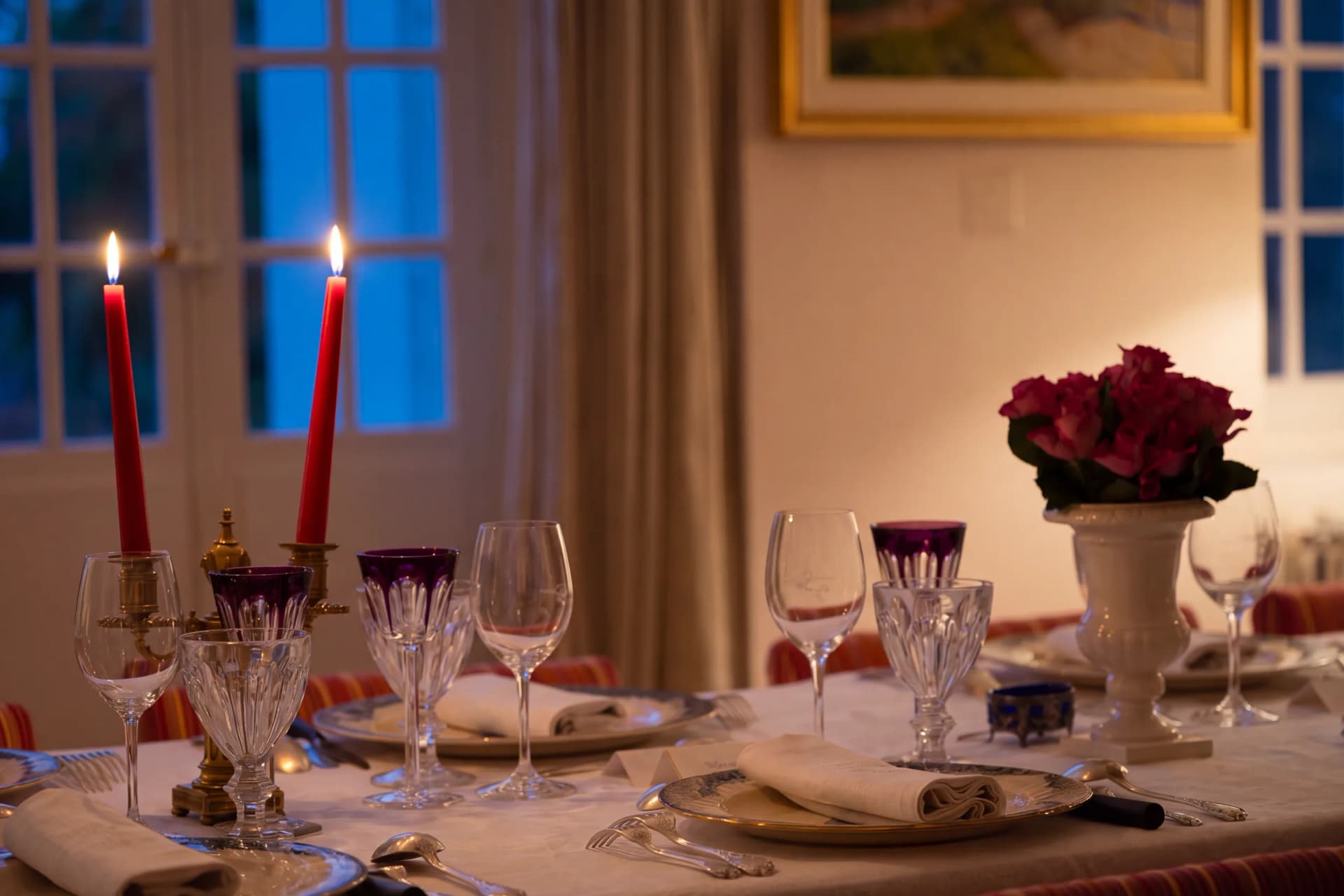 Le soir, devant les portes-fenêtres bleues de la nuit tombante : deux bougies rouges allumées, des verres en cristal améthyste, des roses dans une vasque blanche sur une table dressée