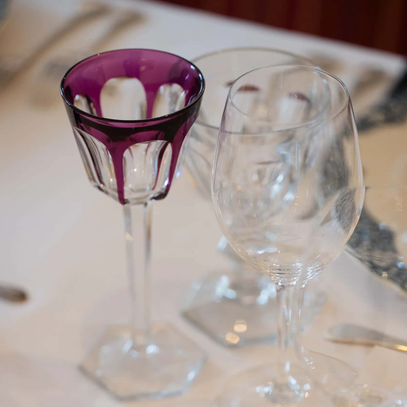 Un verre à vin en cristal taillé améthyste à côté de verres transparents, sur une nappe blanche