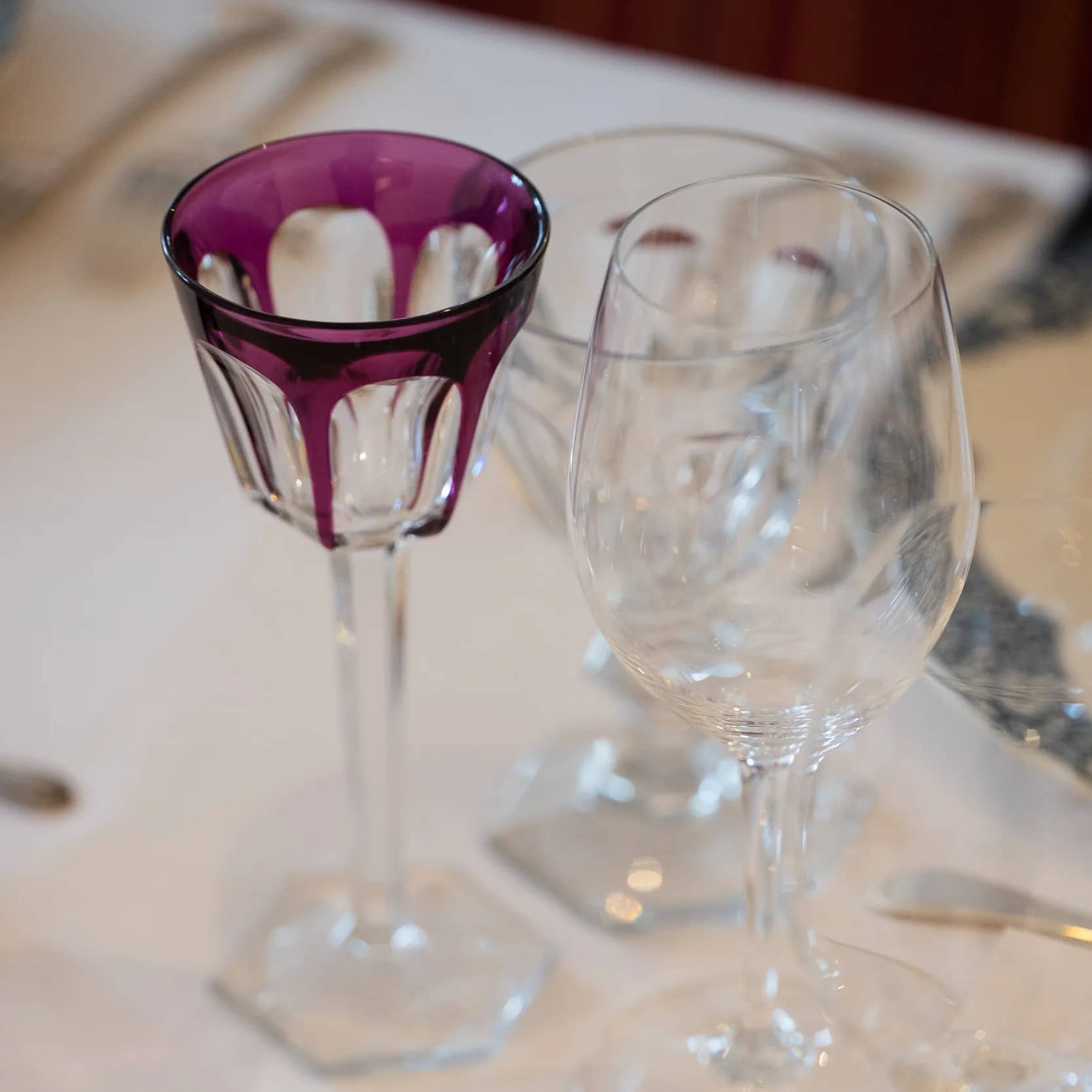 Un verre à vin en cristal taillé améthyste à côté de verres transparents, sur une nappe blanche