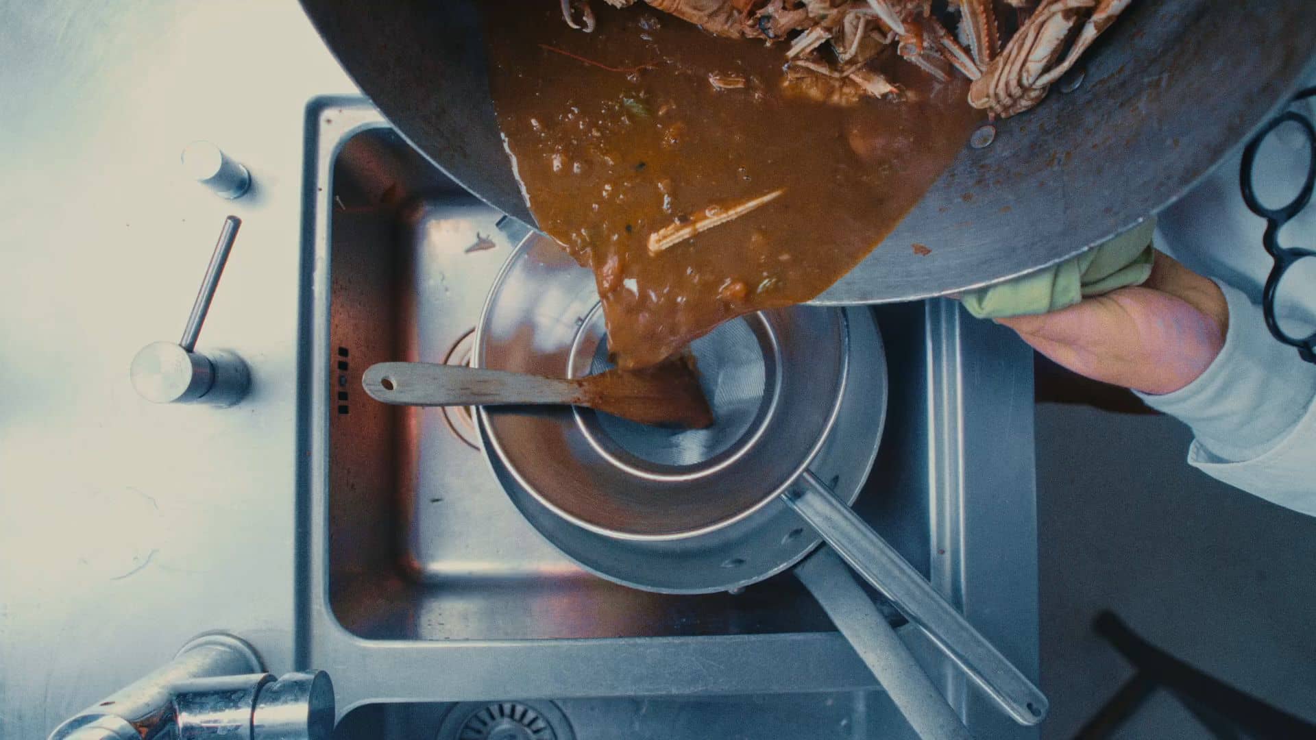 Andres Oppenheim verse une sauce de crustacés à travers un chinois, au-dessus d'une casserole, dans la cuisine de la maison