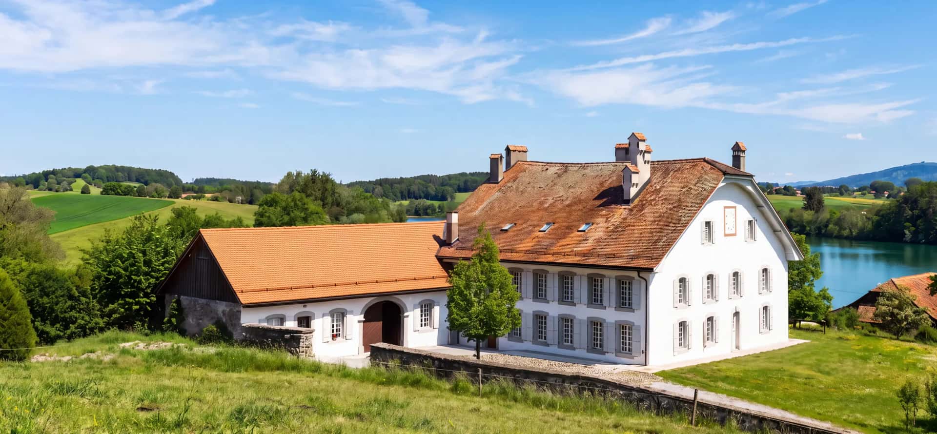 La maison de maître et son jardin un jour d'été : la prairie au premier plan, la pelouse et le Lac de Bret à droite