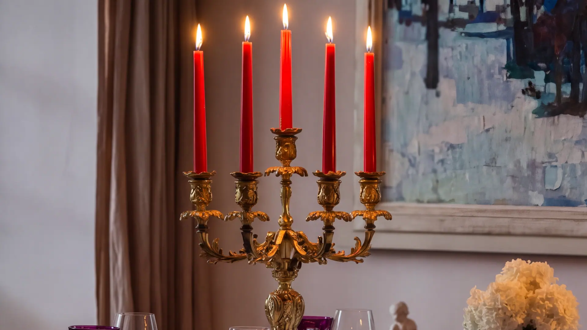 Le grand chandelier doré de la salle à manger de la maison, ses bougies rouges allumées, un bouquet blanc et des verres en cristal